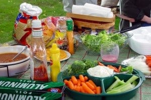 Picnic table with food, condiments, and accoutrements.