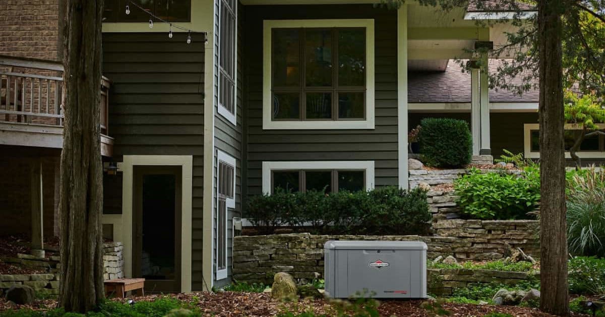 Briggs and Stratton PowerProtect Standby Generator Installed in the backyard of a beautiful two story home amid trees and landscaping.