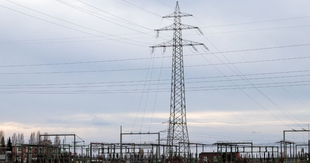 A single power transmission tower stands beside a large power distribution substation