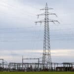 A single power transmission tower stands beside a large power distribution substation