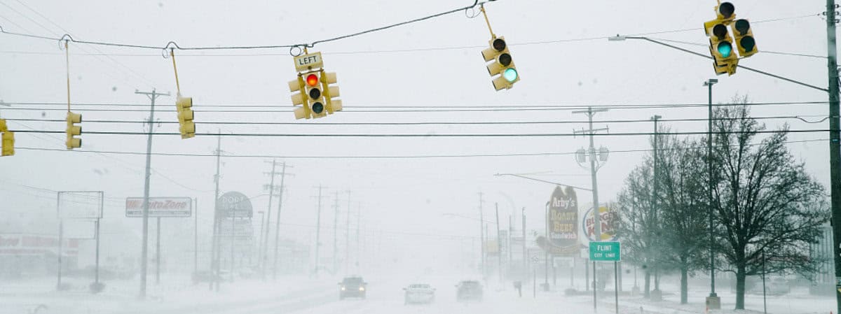 Traffic lights sway to the right during a strong winter cyclone affecting more than half the USA from Texas north and northwest to New England. The street is snow covered, and visibility reduced to less than a block as heavily falling snow obscures local business signs.