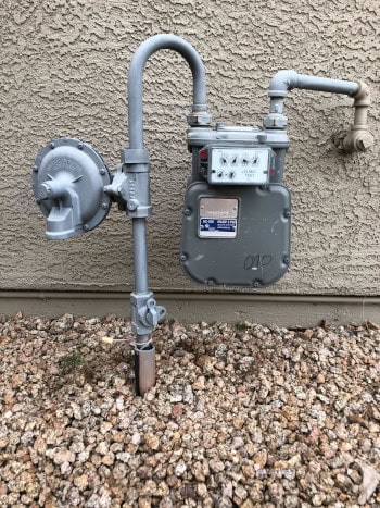 Natural Gas Meter with Regulator on the left, dial on the meter, underground pipe and entry to home.